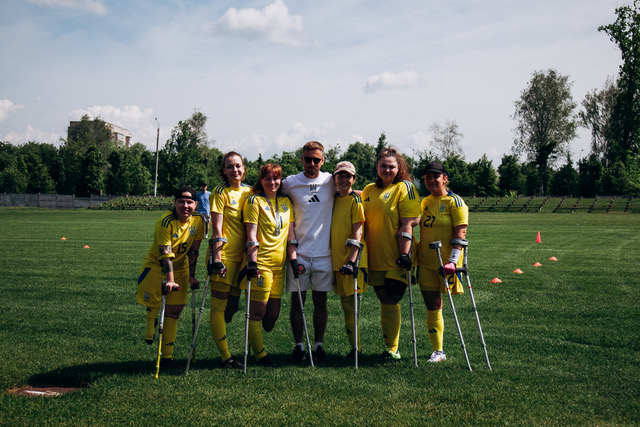 An amputee football team on a grass pitch, standing together with crutches